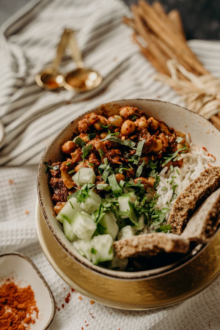 Tasty vegan bowl with chickpeas, rice, cucumber, and herbs on a rustic table.